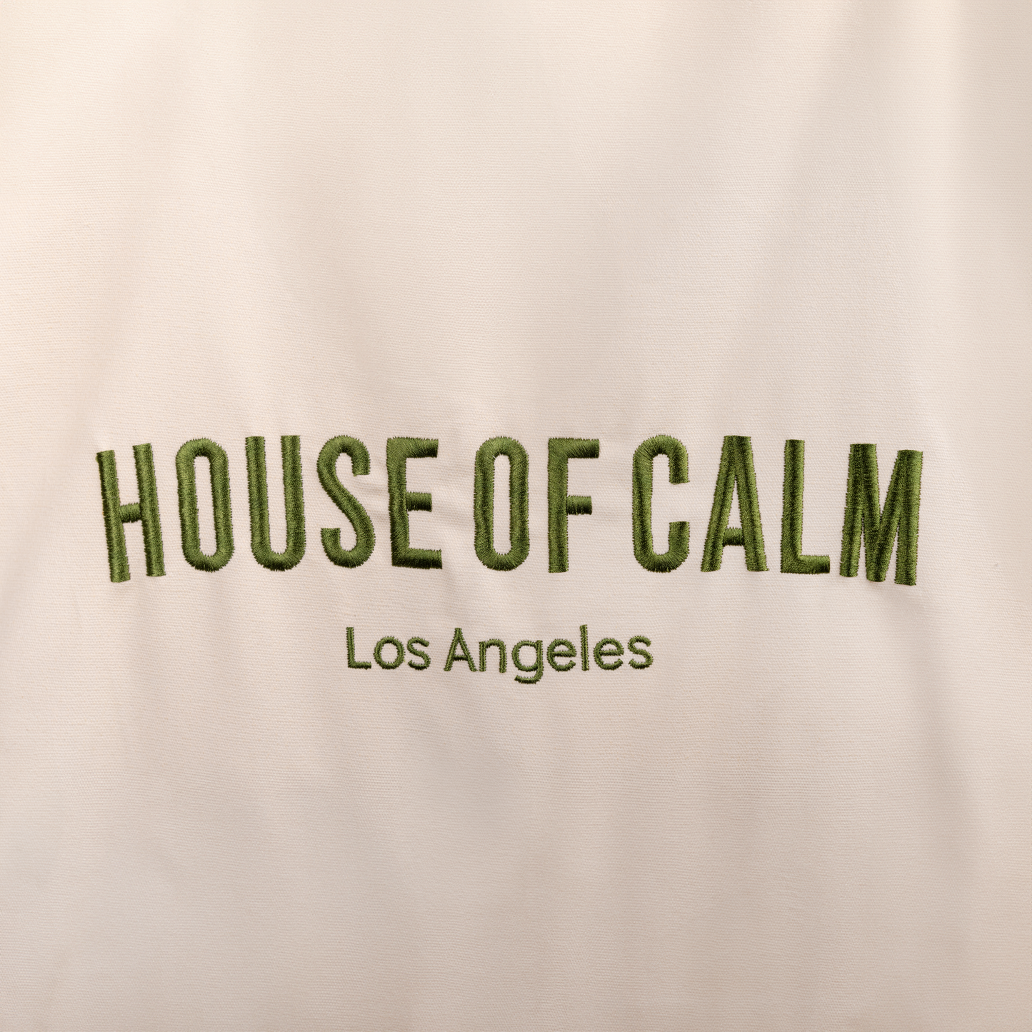 Close-up of embroidered House of Calm logo on natural cotton tote bag